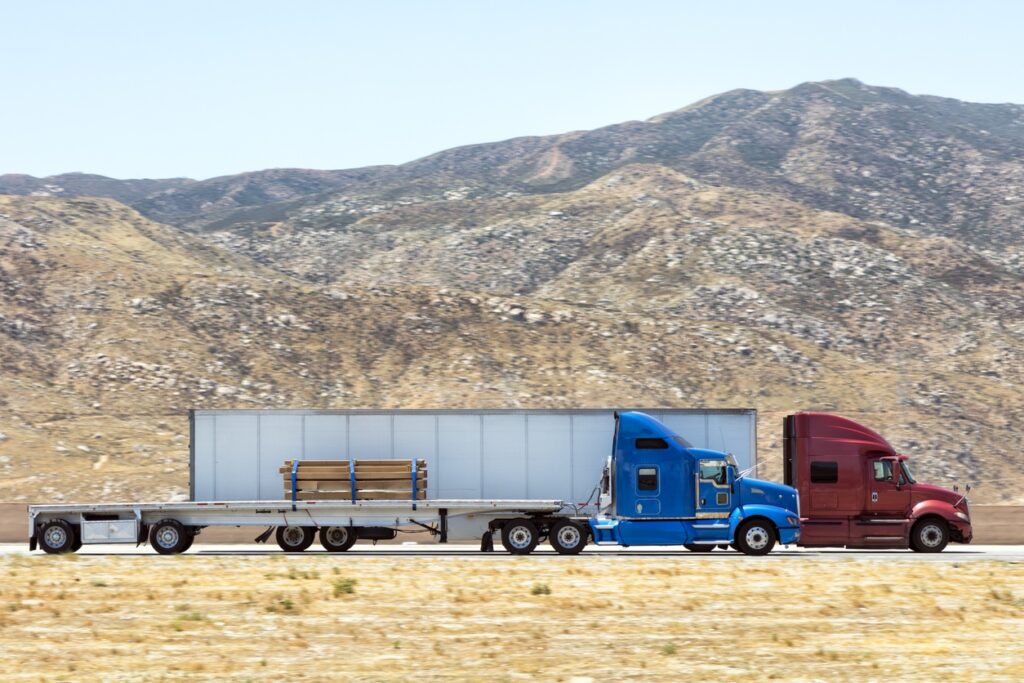 Fast and powerful heavy-lift modern semi trucks with a full size trailer at the turn of mountain scenic highway, blurred motion, western USA, California.