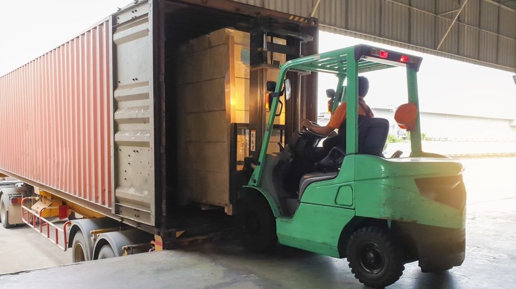 Forklift driver loading goods pallet into the truck container, freight industry warehouse logistics and transport