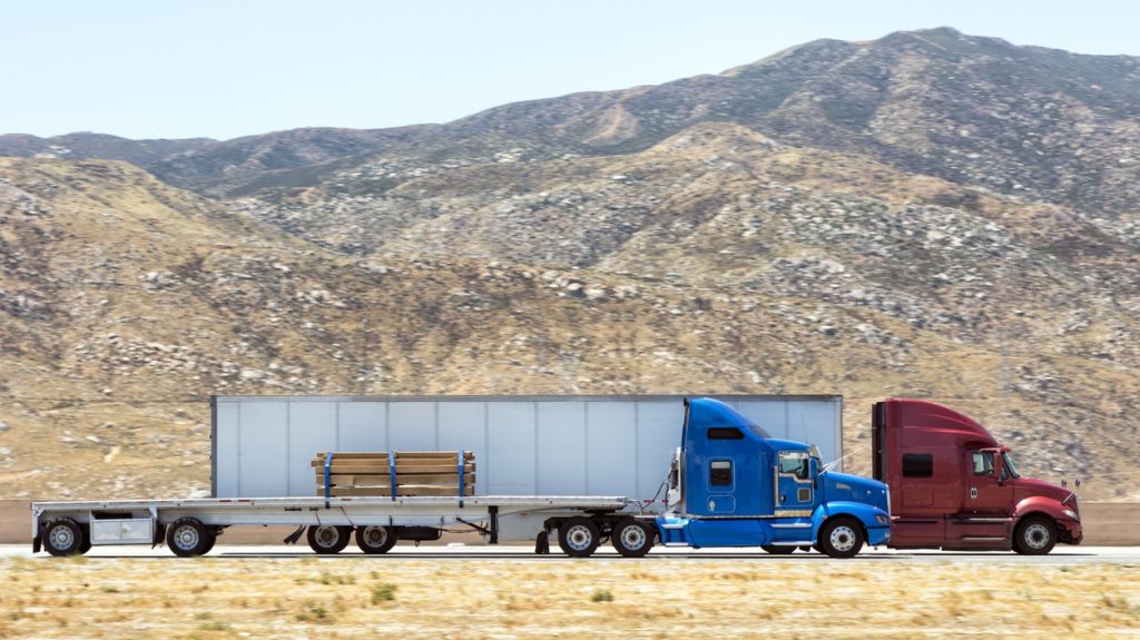 Fast and powerful heavy-lift modern semi trucks with a full size trailer at the turn of mountain scenic highway, blurred motion, western USA, California.